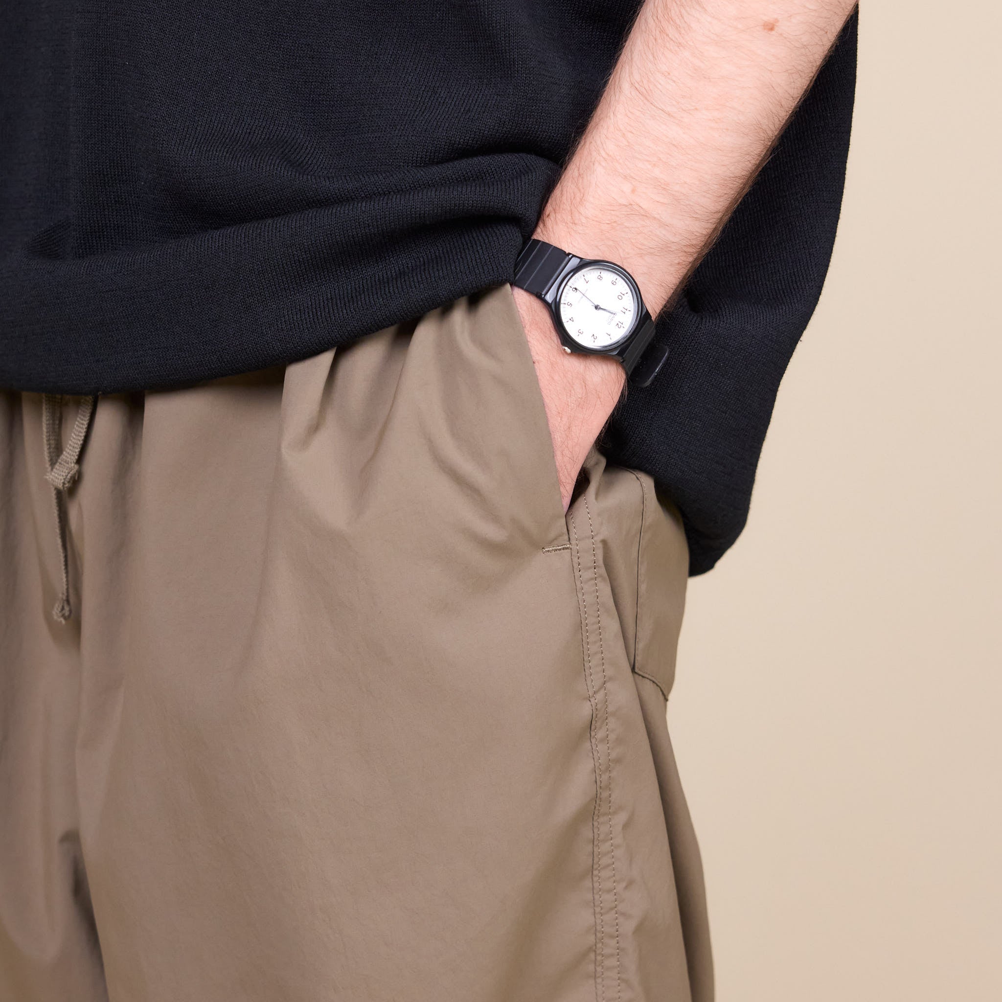 a man putting his hand into the pocket of his pair of Still by Hand Airy Wide Trousers in a Khaki colour with his watch showing on a cream background.