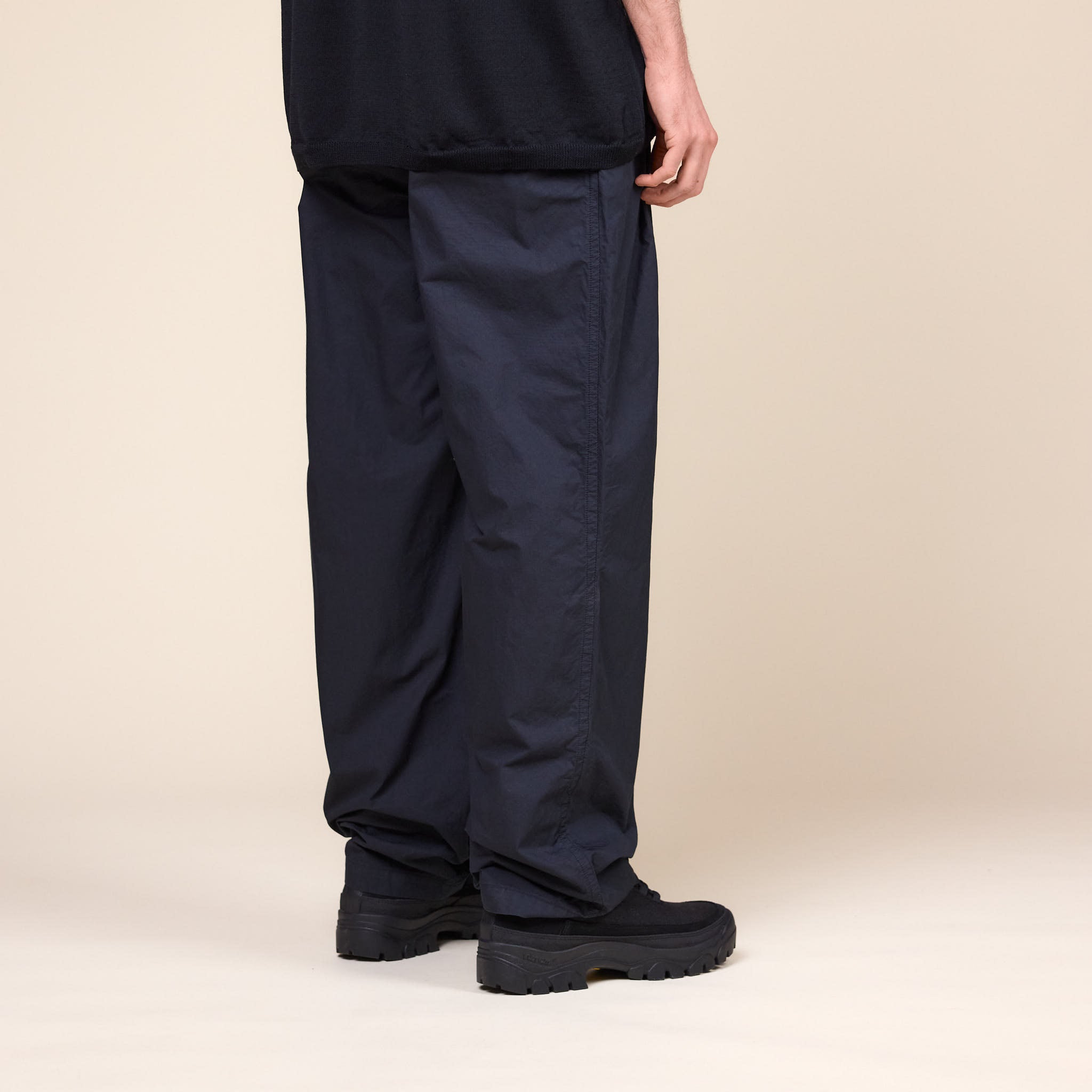 A Man wearing a pair of Still by Hand Garment Dye 2 Tuck Pants in Ink Black colour and a pair of Tarvas Easy Hikes Shoes on a cream background.